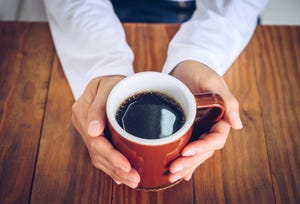 someone hands holding a mug of black coffee before drinking