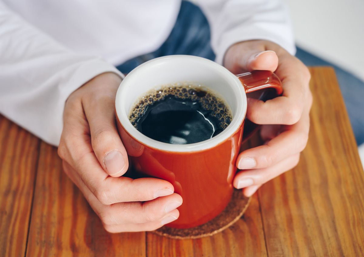someone hands holding a mug of black coffee before drinking