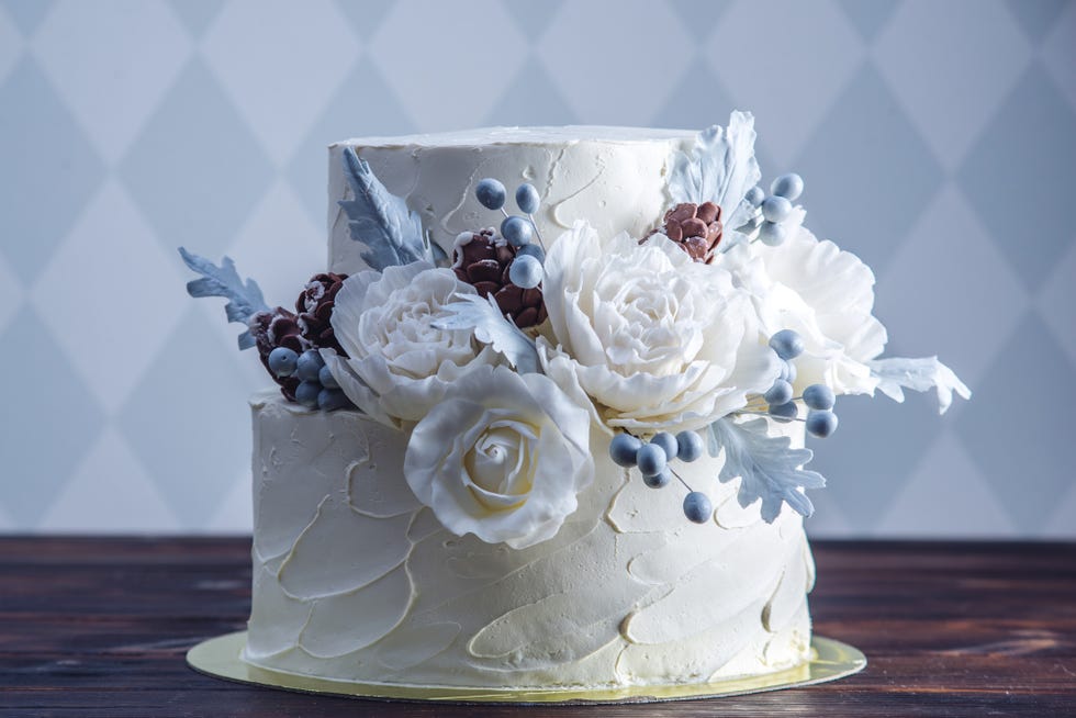 delicate white two tiered wedding cake decorated with an white and blue icing and floral accents