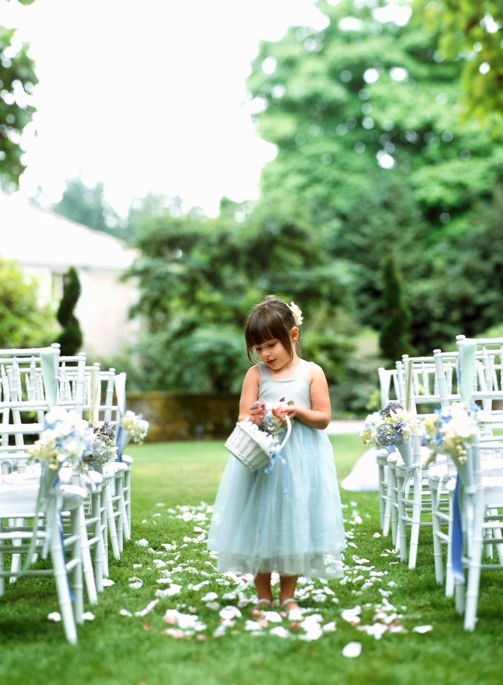 young flower girl in a pale blue dress holding a bouquet of flowers as she walks down an empty aisle