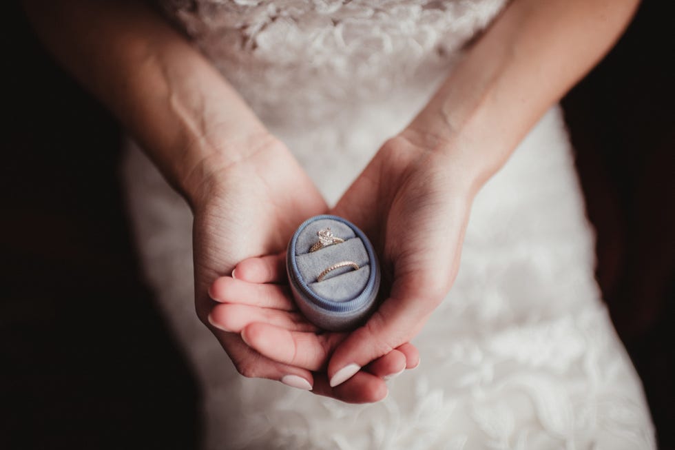 engagement ring and wedding band in a blue velvet box held by the bride