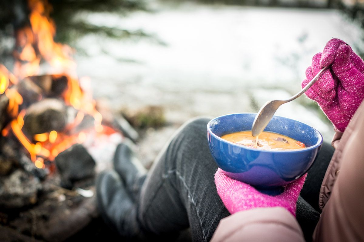 mujer disfrutando de una sopa caliente frente a una hoguera en pleno invierno