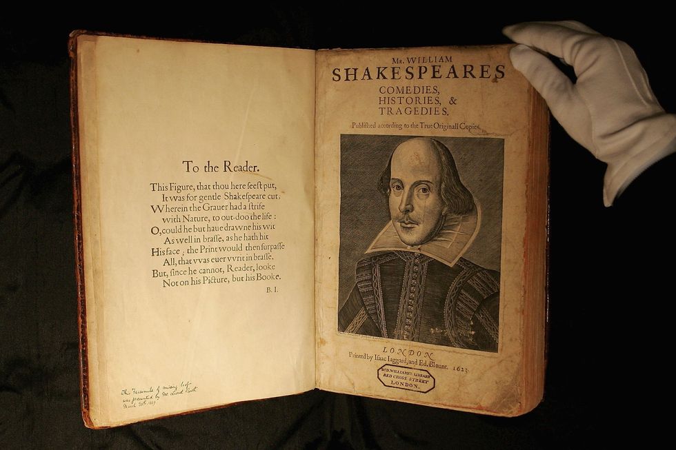 shakespeare’s first folio edition open to the title page with a portrait of william shakespeare on the right page, a white gloved hand touches the top righthand corner of the book