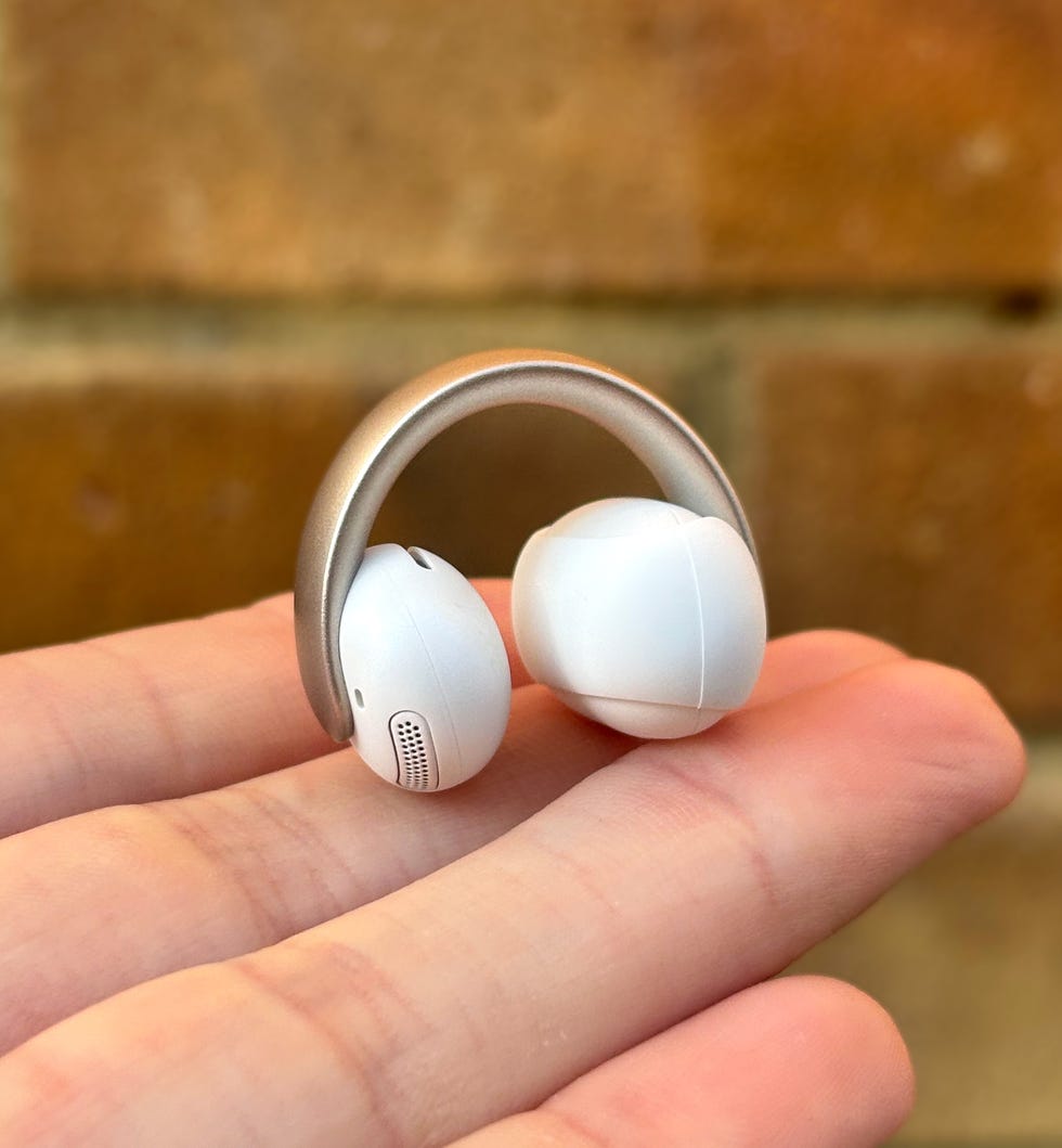 a white clip on style earbud resting on someone's palm against a brick background