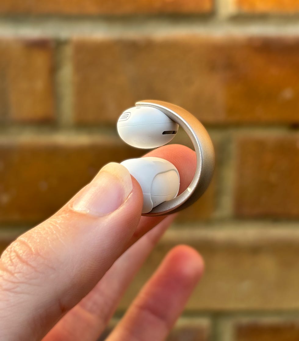 a hand holding a cuff style earbud against a brick wall