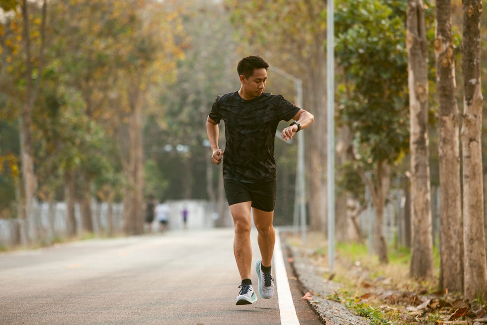 south east asian sportman jogging and checking smart watch between workout jogging outdoor