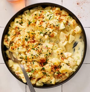 southern potato salad topped with paprika and chopped parsley in a black bowl on a white tile background