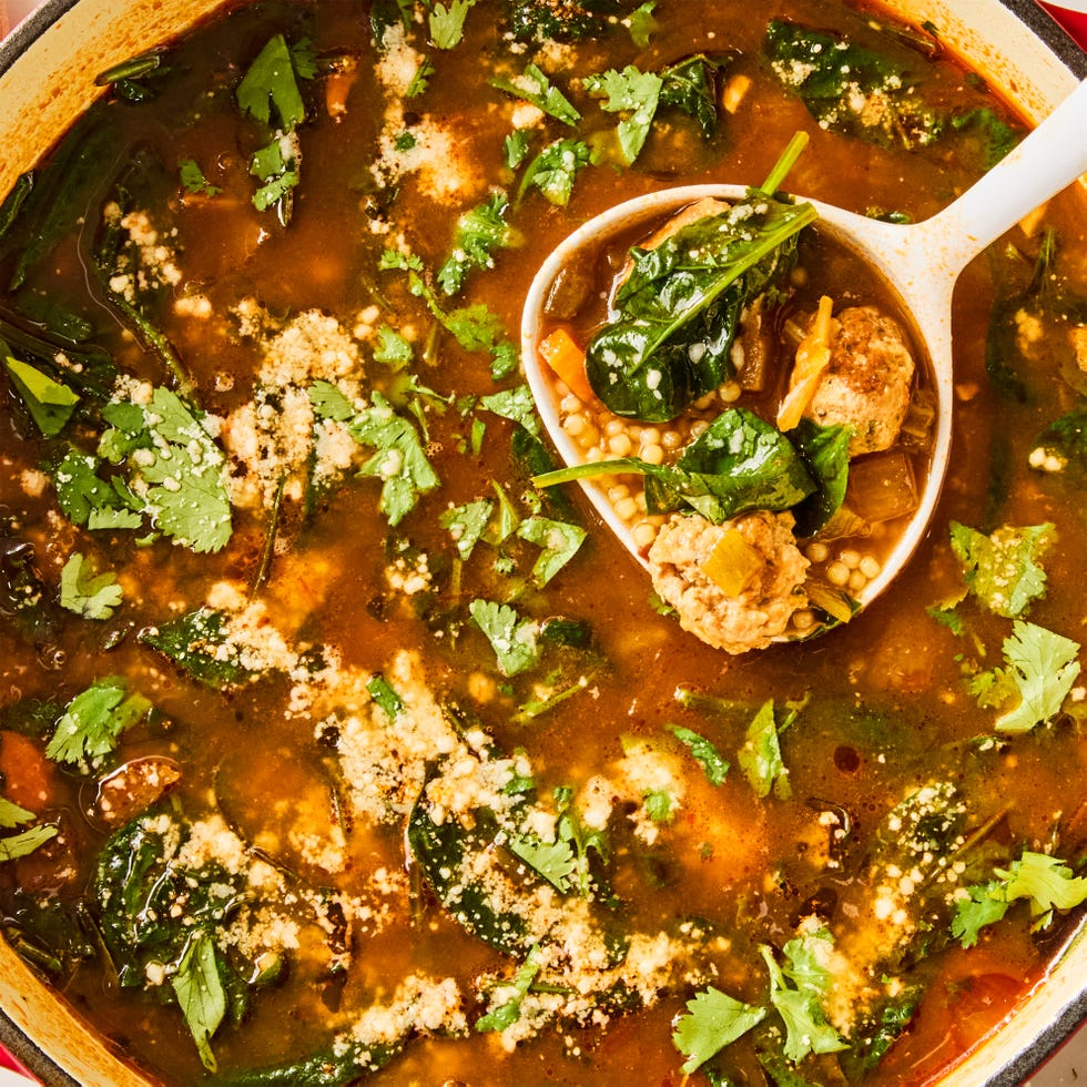 a bowl of soup with pasta, meatballs, spinach, cilantro, and cotija cheese
