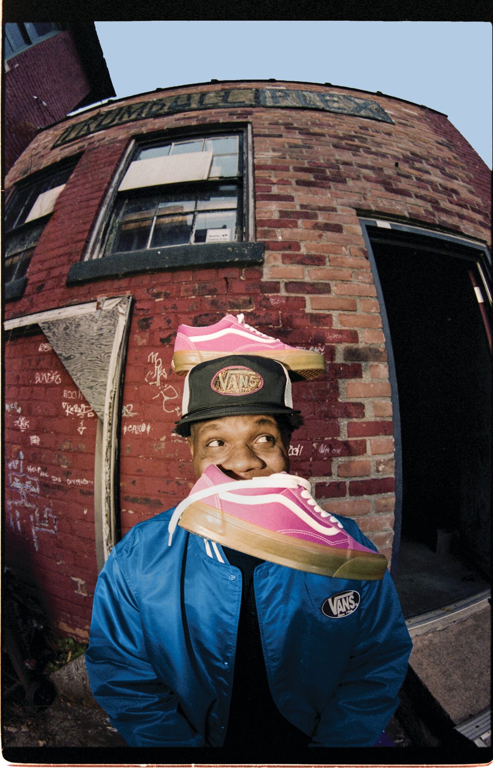 a person wearing a blue jacket with a vans logo holding pink vans sneakers