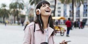 Spain, Barcelona, laughing woman with coffee, cell phone and headphones in the city