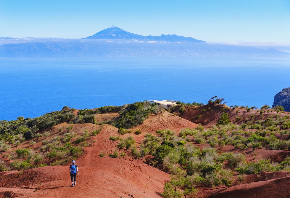 spain, canary islands, agulo, female backpacker hiking toward mirador de abrante observation point with mount teide in distant background