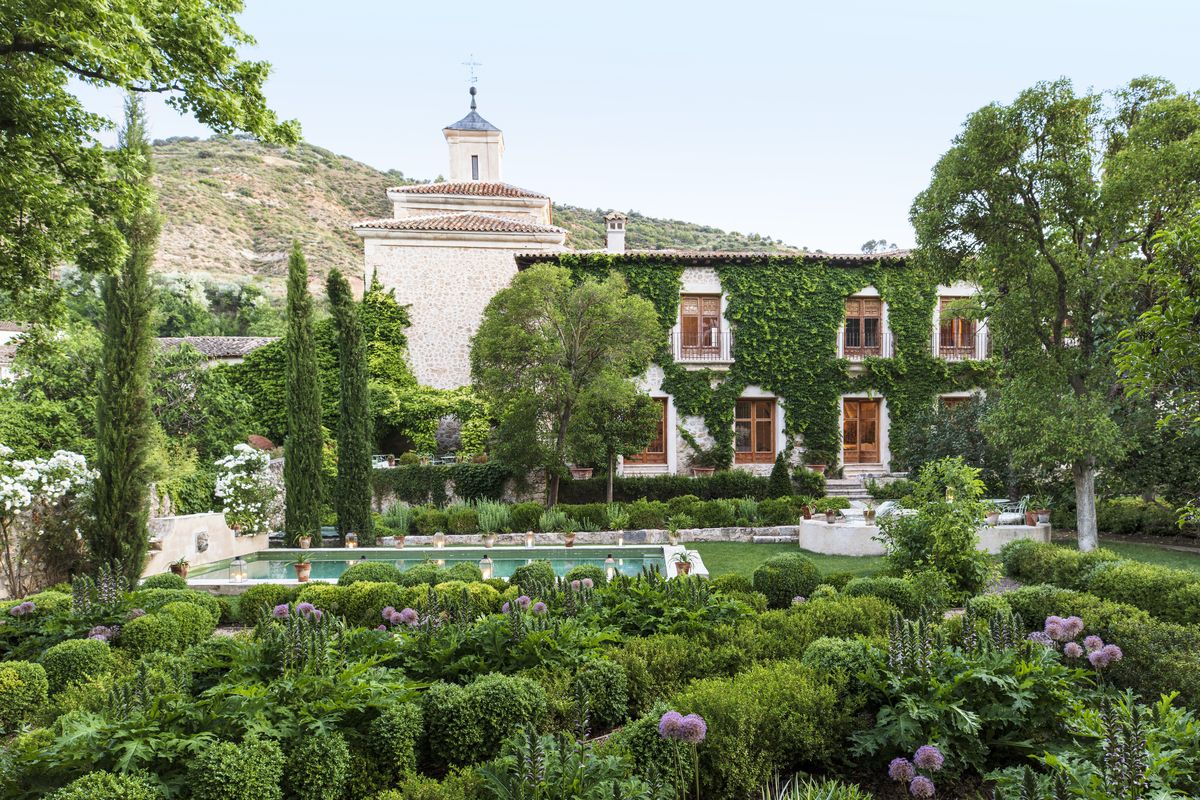 17th century palace in tendilla, spain design by Álvaro sampedro beyond a lush oasis dotted with italian cypress and linden trees, boston ivy climbs the spanish palace’s facade