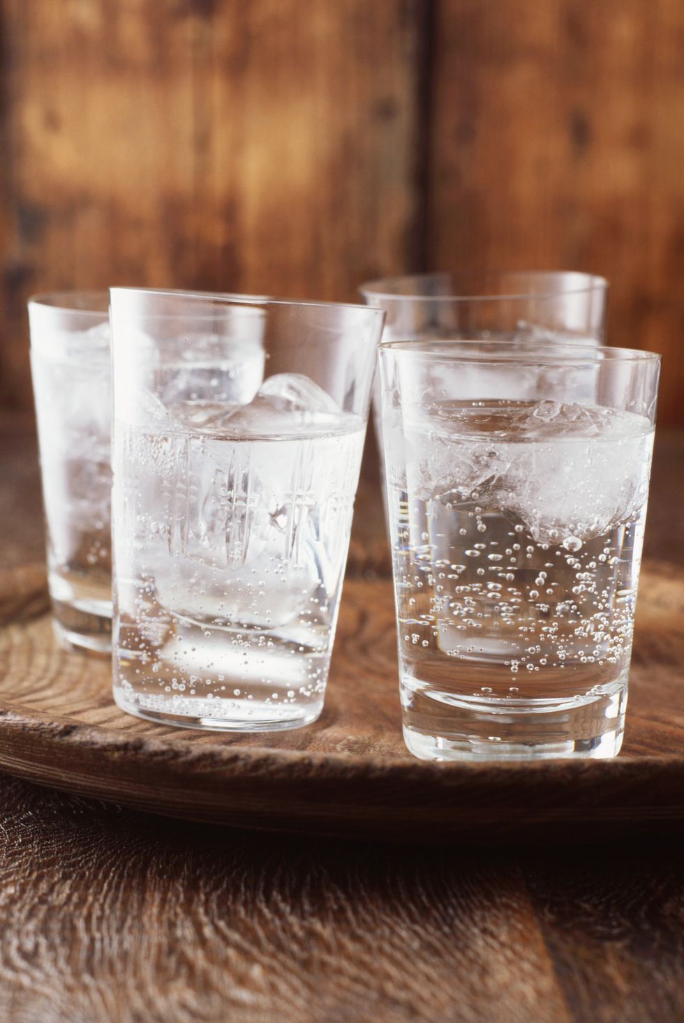 sparkling water in drinking glass with ice on vintage wooden plate