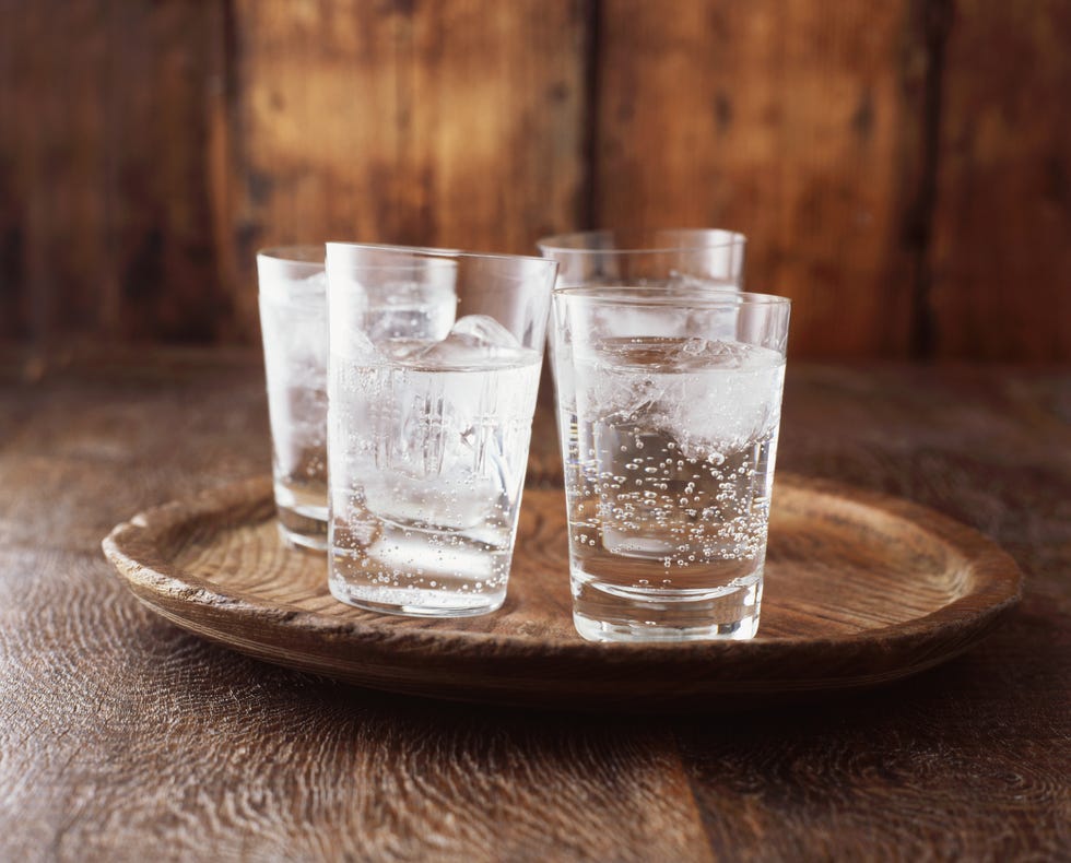 sparkling water in drinking glass with ice on vintage wooden plate