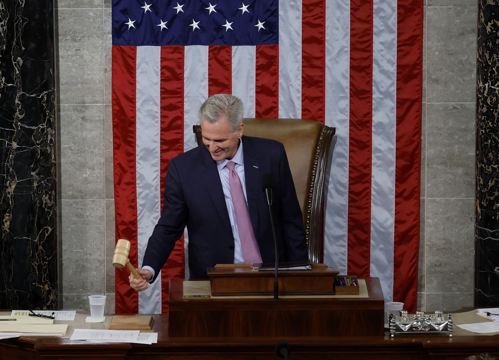 kevin mccarthy hits the gavel in the house chamber, he stands behind a wooden lectern and in front of a large brown leather chair and part of a hanging american flag