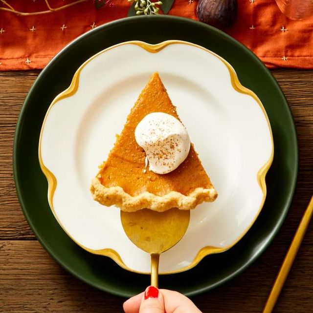 a hand holding a serving knife with a slice of pumpkin pie on it