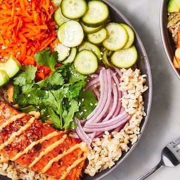 a rice bowl topped with salmon, red onion, cucumbers, carrots, avocado, and cilantro