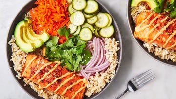 a rice bowl topped with salmon, red onion, cucumbers, carrots, avocado, and cilantro