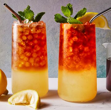 glass with lemonade on the bottom and iced tea on the top with crushed ice, a lemon squeeze and mint