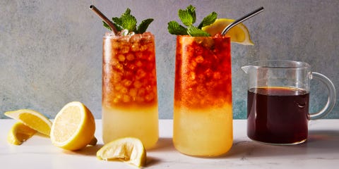 glass with lemonade on the bottom and iced tea on the top with crushed ice, a lemon squeeze and mint