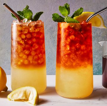 glass with lemonade on the bottom and iced tea on the top with crushed ice, a lemon squeeze and mint