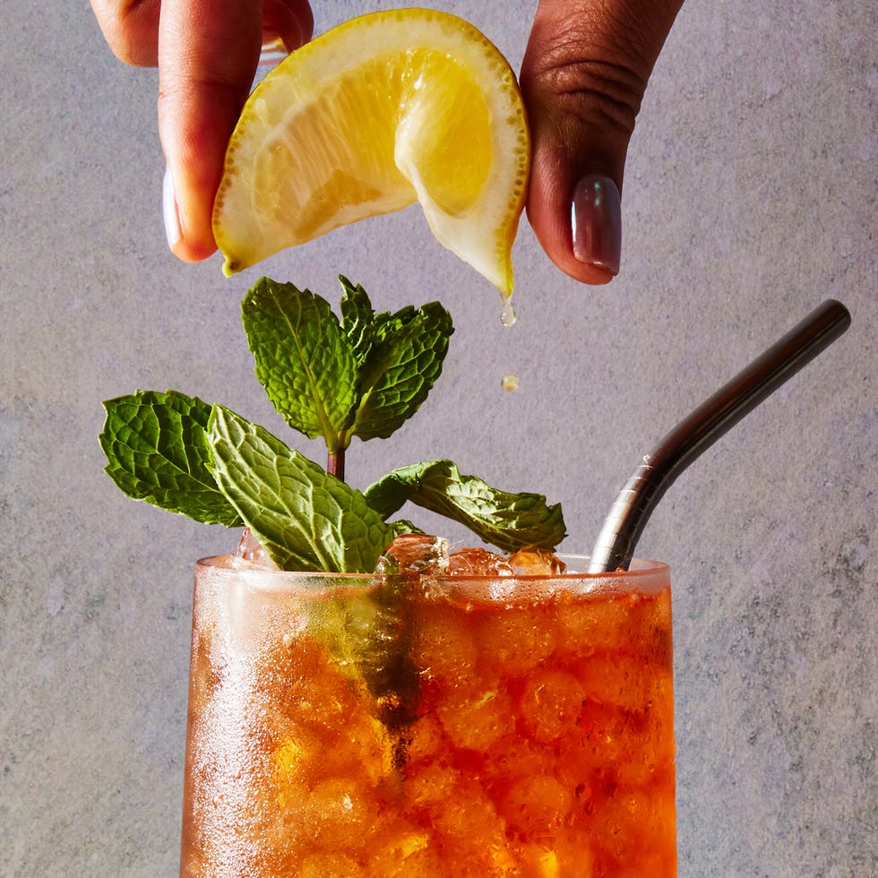 glass with lemonade on the bottom and iced tea on the top with crushed ice, a lemon squeeze and mint