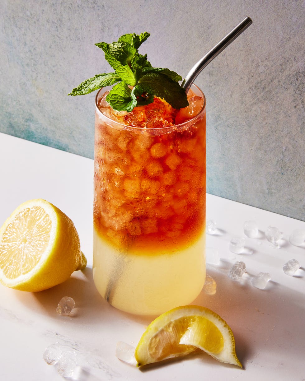 glass with lemonade on the bottom and iced tea on the top with crushed ice, a lemon squeeze and mint