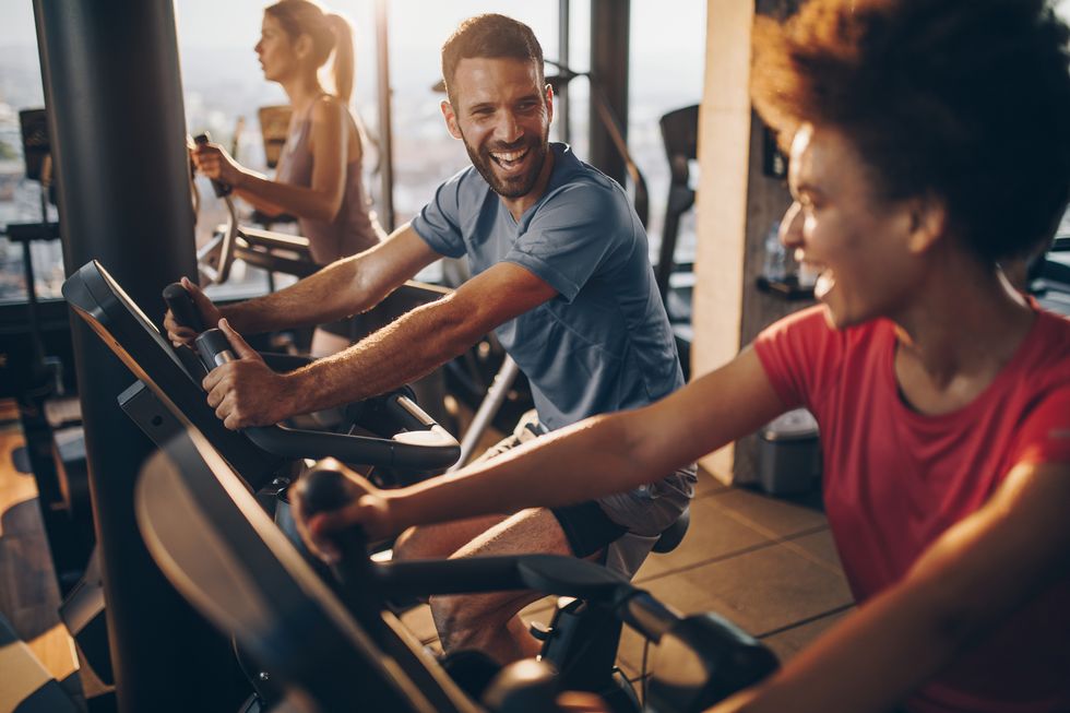 Cheerful male athlete talking to his friend on spinning training in a health club.