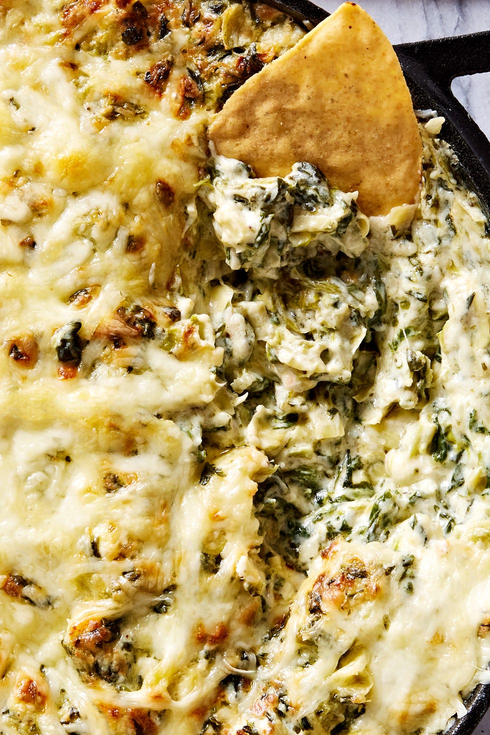 spinach artichoke dip in a cast iron skillet served with tortilla chips