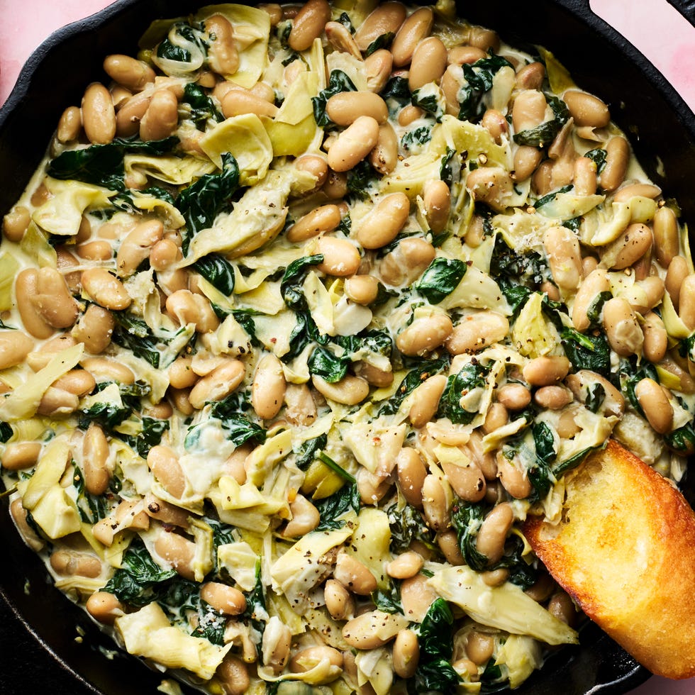 white beans in a skillet with spinach, artichokes, and cheese