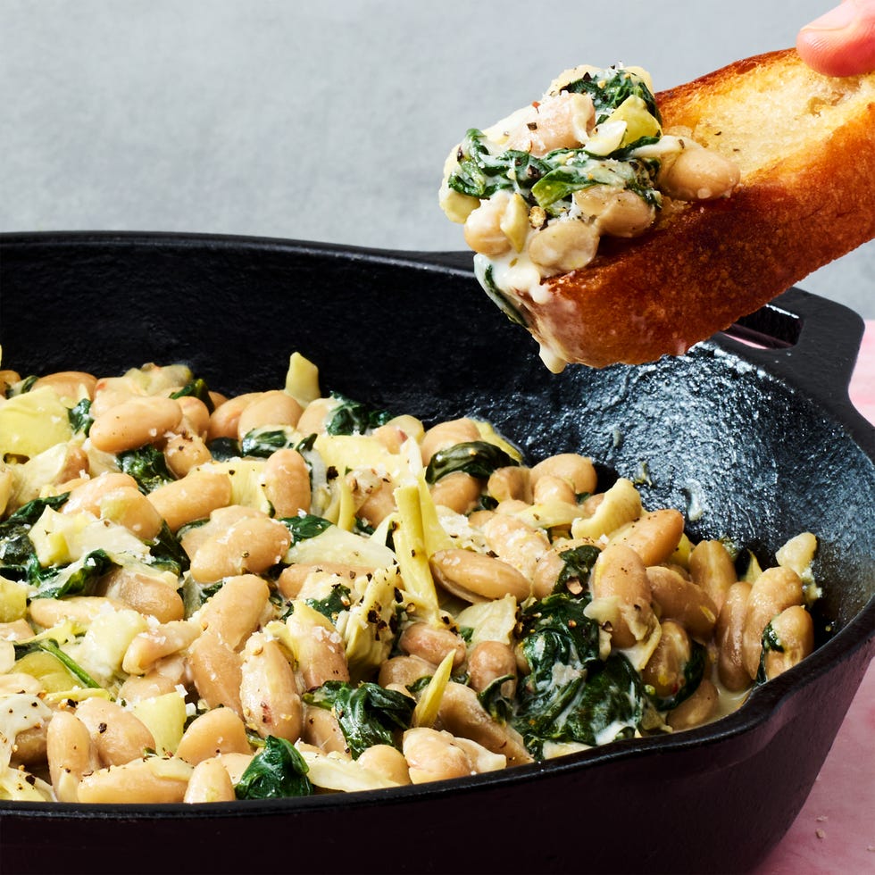 white beans in a skillet with spinach, artichokes, and cheese