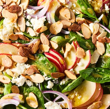 spinach in a bowl topped with sliced apples, sliced almonds, red onions, and crumbled feta