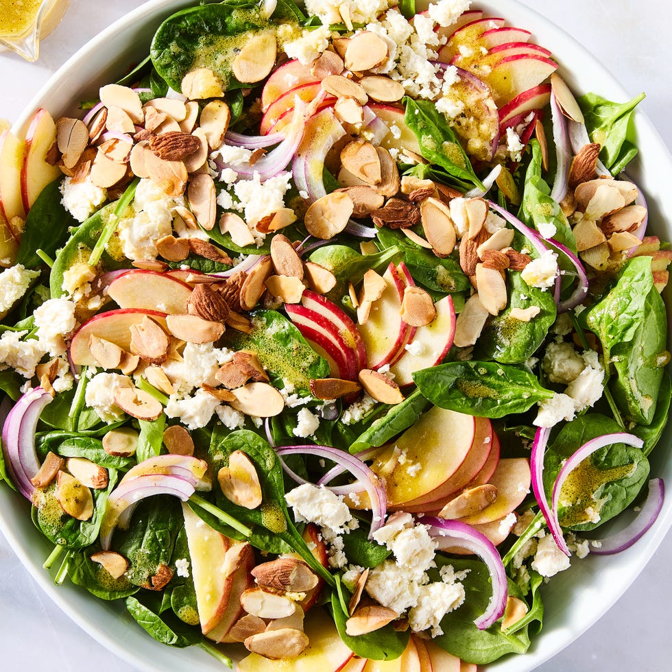 spinach in a bowl topped with sliced apples, sliced almonds, red onions, and crumbled feta
