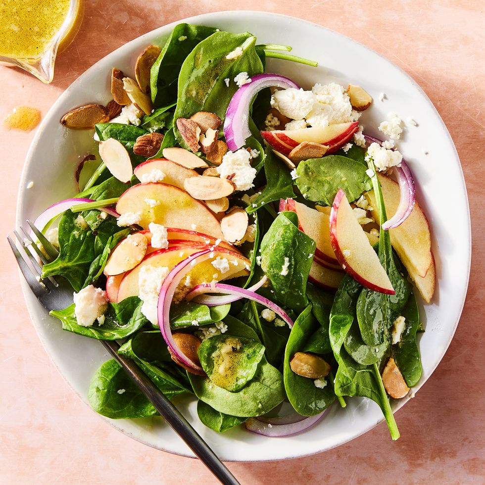 spinach in a bowl topped with sliced apples, sliced almonds, red onions, and crumbled feta