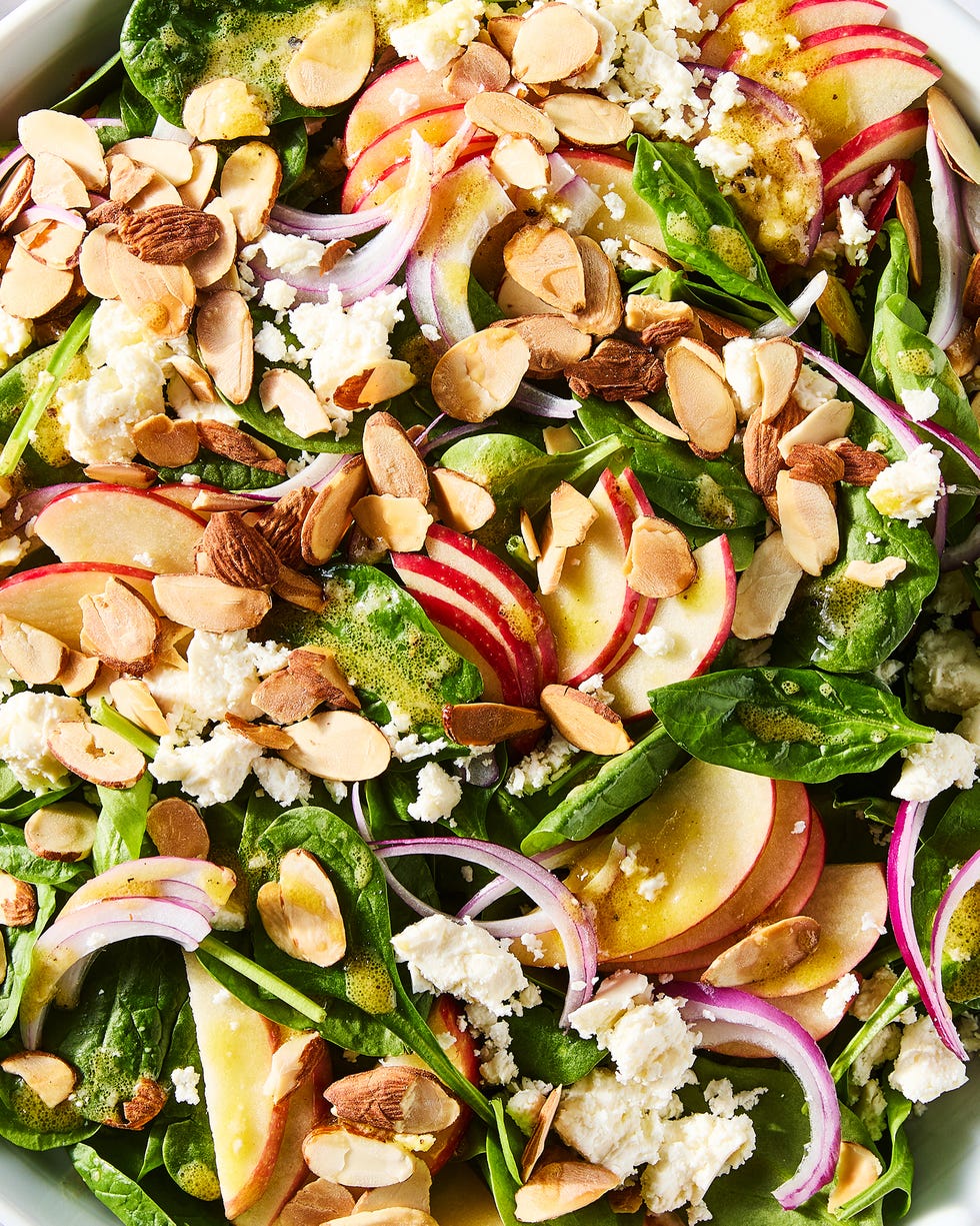 spinach in a bowl topped with sliced apples, sliced almonds, red onions, and crumbled feta