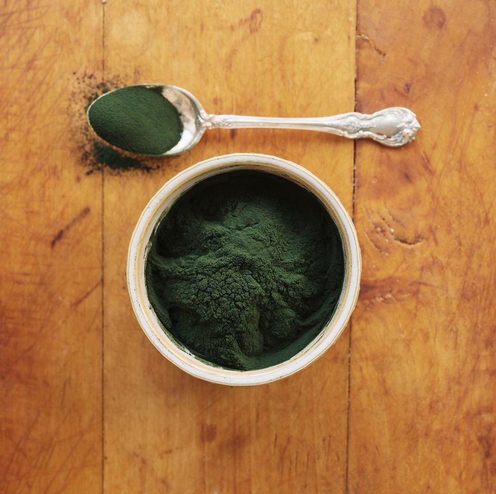 spirulina in bowl and spoon full against wood