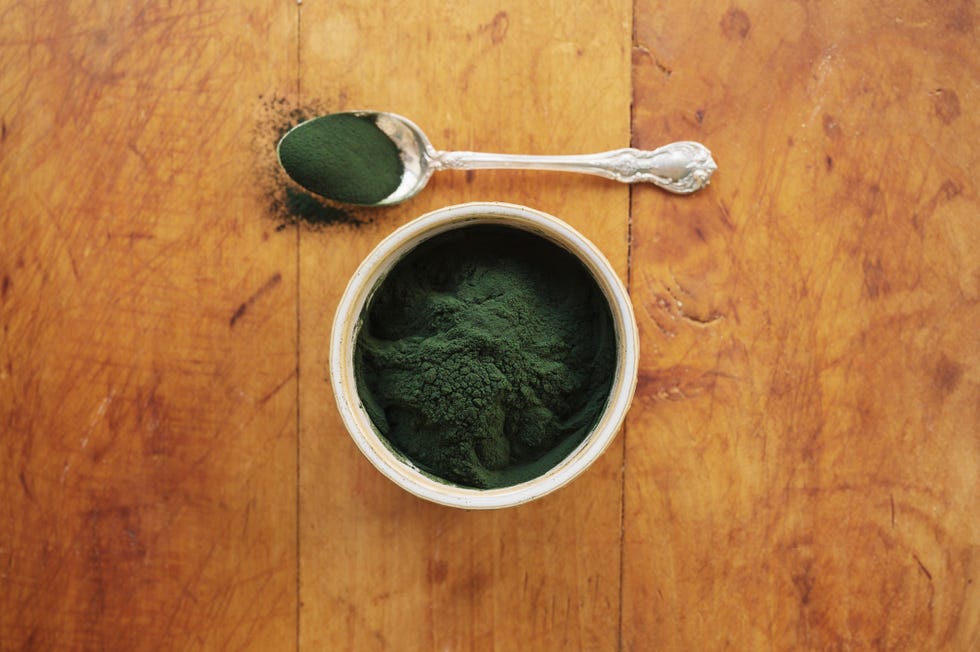 spirulina in bowl and spoon full against wood