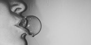 black and white photo shows a woman blowing a spit bubble
