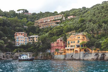 a boat in the water by a hill with buildings on it with lake como in the background