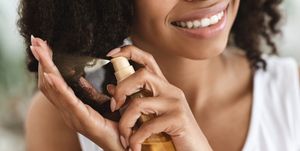 split ends treatment smiling black woman spraying essential oil on curly hair