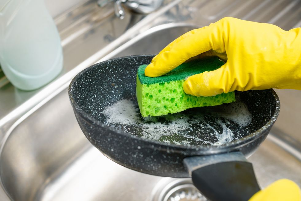 hand with a sponge washes a dirty frying pan under running water