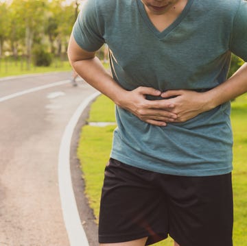 sport man holding abdomen with his hands in stomach pain after running workout at park health care concept