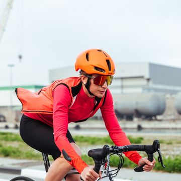 wielrenster met oranje helm en rode fietsjack en oranje windstopper fietsend met windstopper open geritst