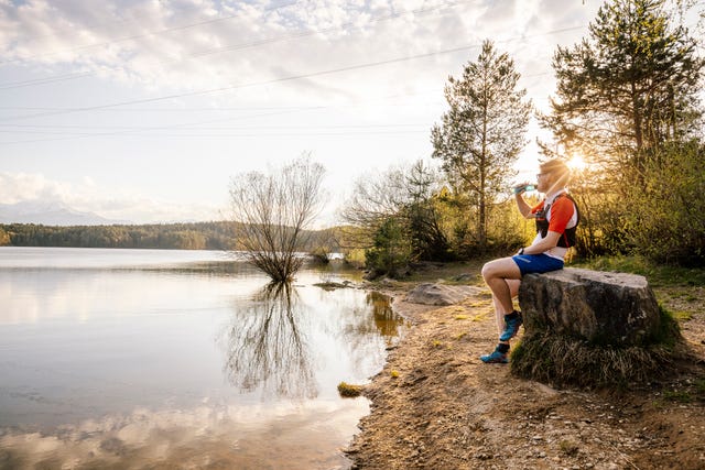 sportive man sitting on a rock at the lakeside at sunset, forstsee, carinthia, austria