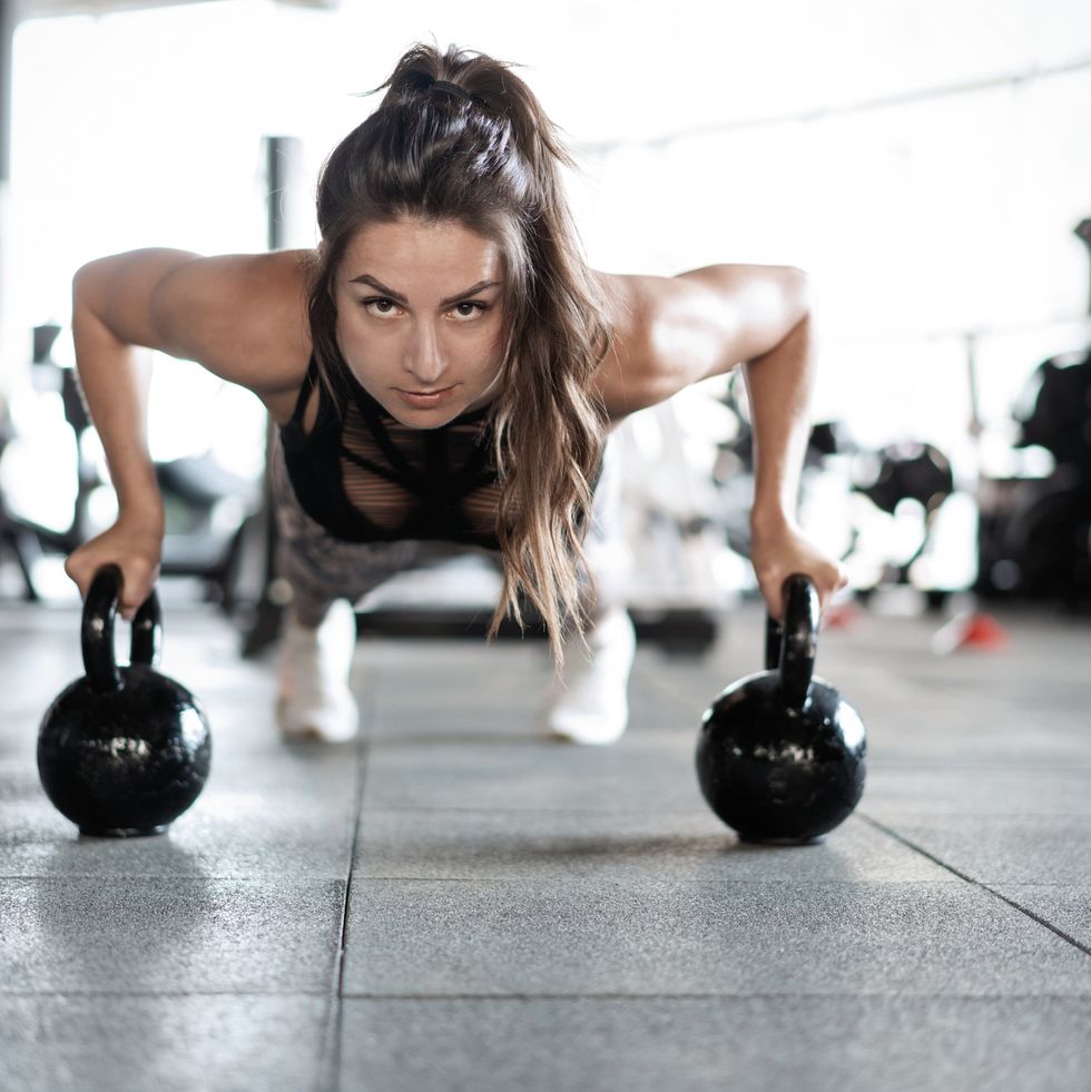 sportive woman doing push ups in the gym using kettlebells