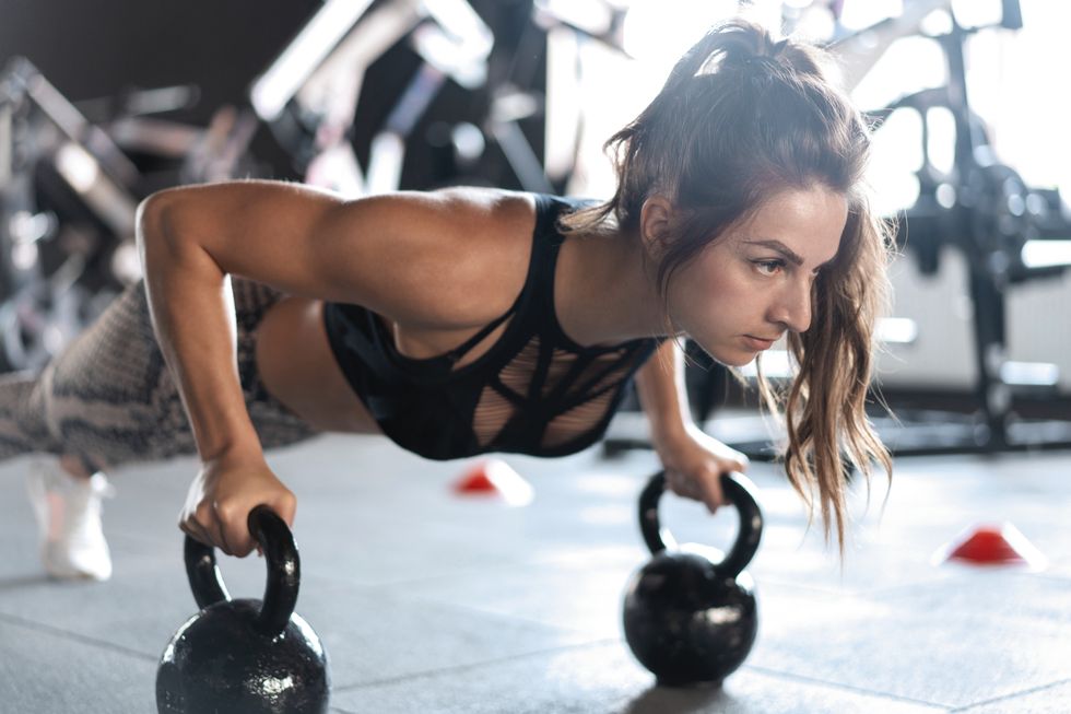 sportive woman doing push ups in the gym using kettlebells