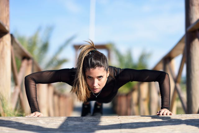 sportive woman doing pushups on wooden bridge