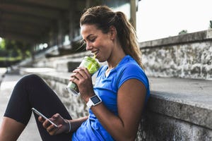 sportive young woman sitting on grandstand with cell phone and drinking mug