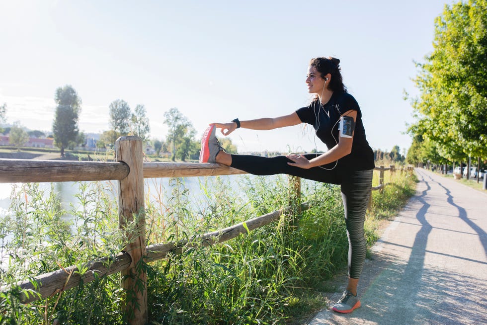 Sportive young woman stretching her leg at the riverside