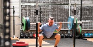 sportsman doing back squat exercise with barbell in gym